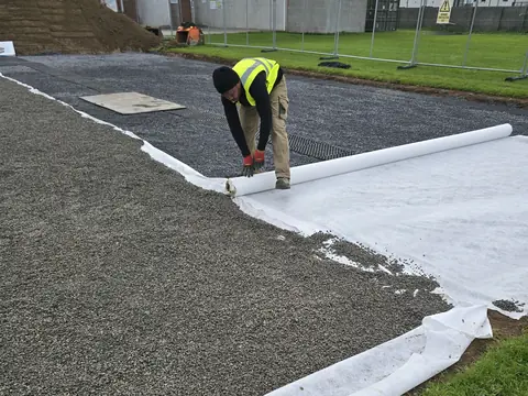 One of our crew unrolling the white geotextile, with finer stone already spread over it