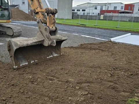 The digger's bucket spreading soil back over the geotextile
