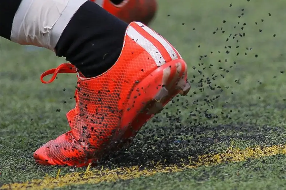 A football boot kicking loose black rubber crumb out of a synthetic pitch