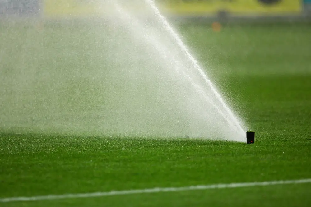 A pop-up sprinkler watering the grass of a sports pitch