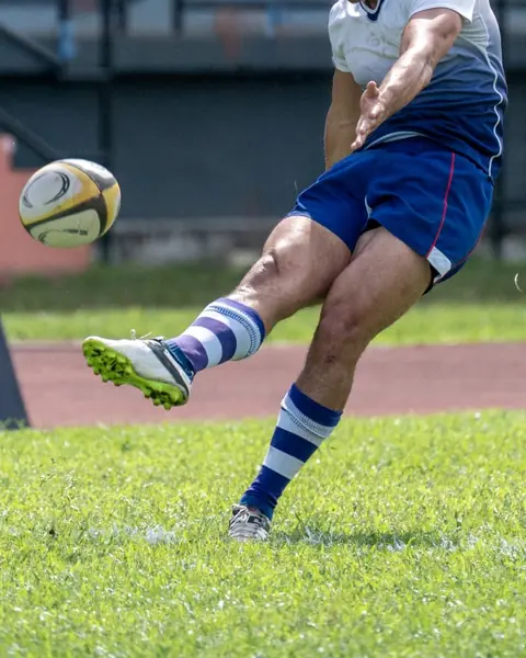 A rugby player kicking the ball off the grass