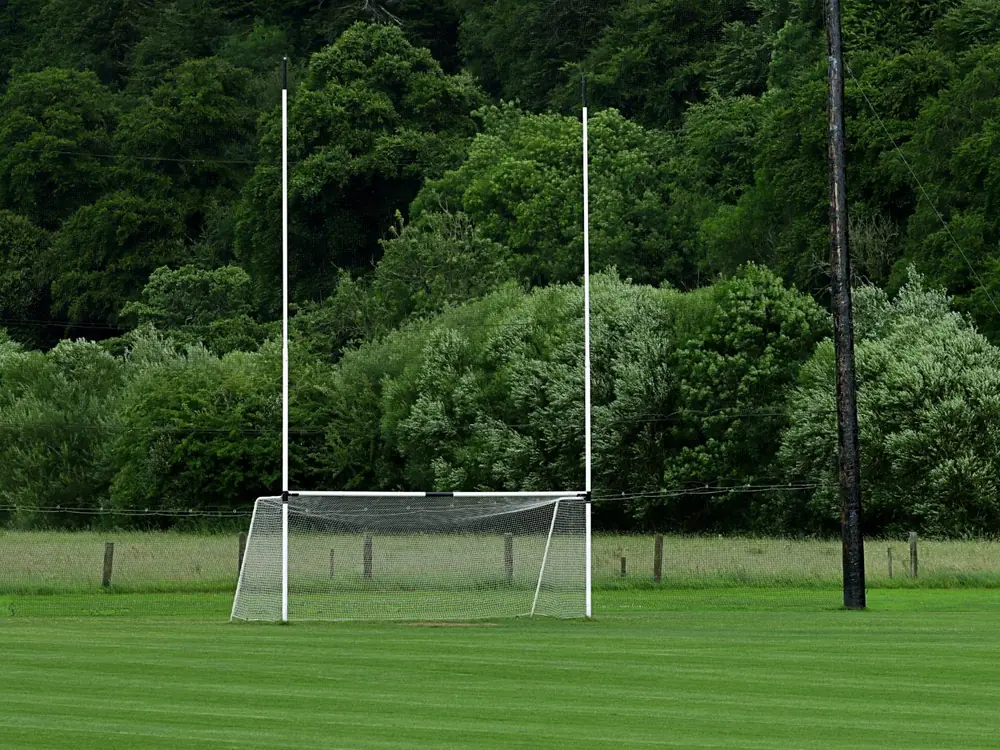 Gaelic football goalposts with a net, trees behind